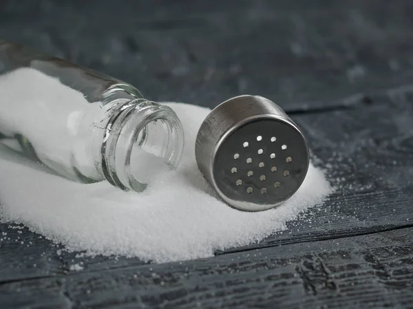 Witte zout gegoten uit de open zout shaker op houten tafel. — Stockfoto