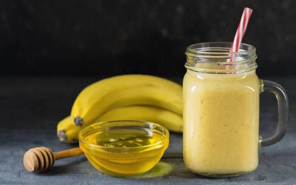 Sebuah smoothie mangga, pisang, madu dan sereal pada latar belakang hitam. Semangkuk madu . — Stok Foto