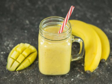 Bir yüzlü mango, muz, bal ve siyah bir taş masada Mısır gevreği. Bir kase bal.