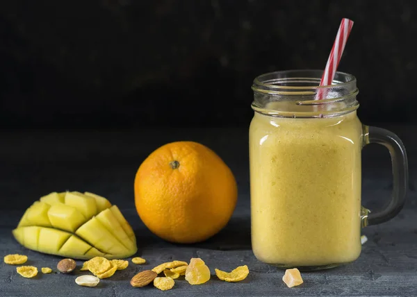 Sebuah smoothie mangga, pisang, madu dan sereal pada latar belakang hitam. Kacang dan serpihan berserakan di atas meja . — Stok Foto
