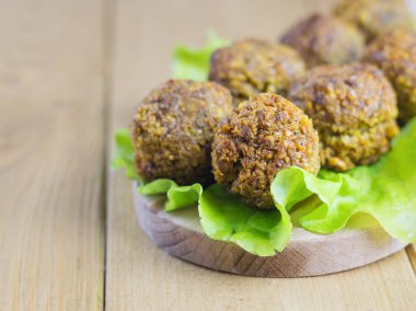 Taze bir salata yaprağı kahverengi ahşap bir masa üzerinde bir kesim tahtası üzerinde falafel yaptı.