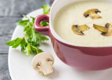 Taze hazırlanmış beyaz tabakta mor bir kase mantar kremalı çorba.