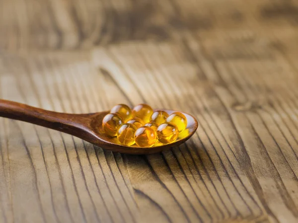 Cápsulas de óleo de peixe em uma colher de madeira em uma mesa de madeira. Medicina tradicional . — Fotografia de Stock