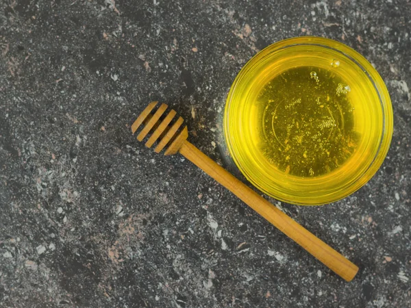 Το μέλι σε ένα γυάλινο μπολ με ένα ξύλινο κουτάλι στο μαύρο πέτρινο τραπέζι. Φρέσκια συγκομιδή του μελιού. — Φωτογραφία Αρχείου