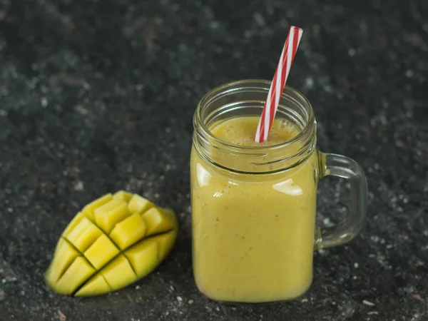 Ein Smoothie aus Mango, Banane, Honig und Müsli auf einem Tisch aus schwarzem Stein. Schneiden Sie eine reife Mango mit einem Getränk. — Stockfoto