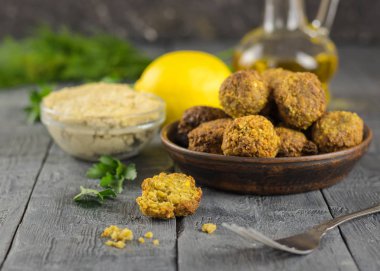 Taze pişmiş kil kase tahin sosu ve yağ ile ahşap bir masa üzerinde falafel.