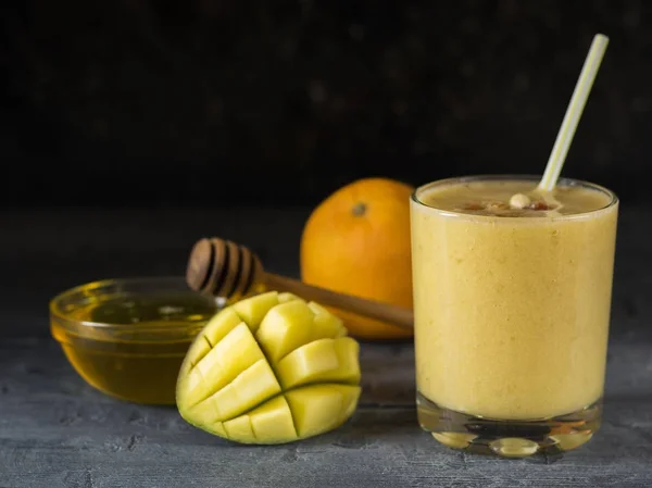 Un batido de mango, plátano, naranja y miel en la mesa oscura en un vaso de precipitados . — Foto de Stock