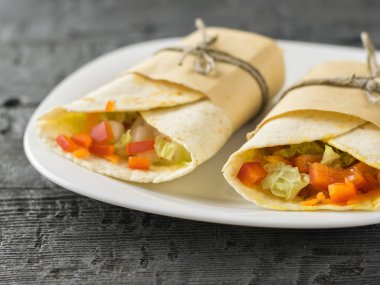 Buğday unu siyah bir masada beyaz kase gelen iki sebze rulo tortilla.