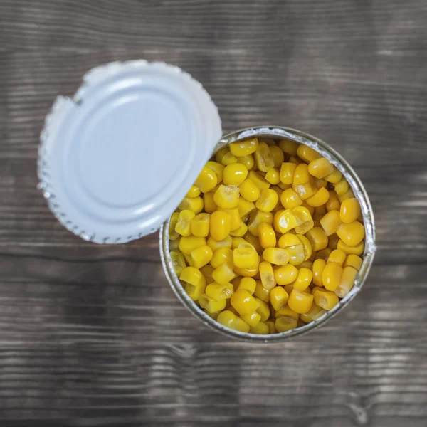 Canned corn in an open aluminum cans on a wooden table. The view from the top.