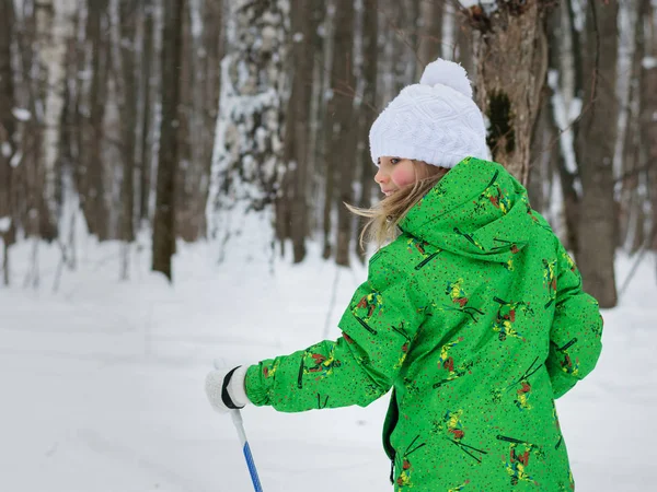 Liten flicka i en ljust grön passar utbildade skidor i skogen. — Stockfoto