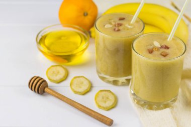 Bir beyaz tahta masada smoothies ile mango, muz, portakal, tatlım, fındık ve tahıl taze yapılmış.