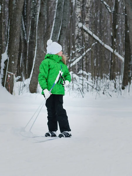 Flickan i den gröna jumpsuit ser tillbaka på sökvägen på skidor. — Stockfoto
