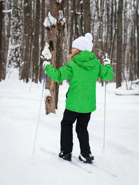 Foto flickor i en grön jacka skidåkning i skogen vinter. — Stockfoto