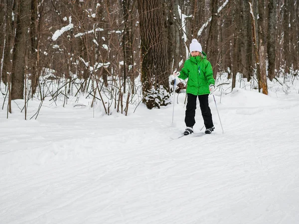 Flickan går på skidor med pinnar i skogen vinter. — Stockfoto