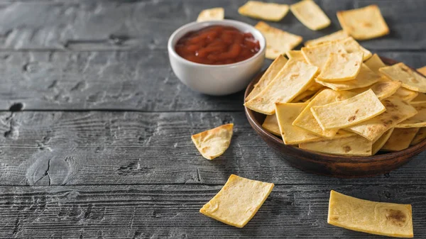 Chips from a Mexican tortilla with tomato sauce on the black wooden table. — Stock Photo, Image