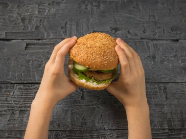 Tablo üzerinde bir çocuğun elinde taze hamburger. Ev yapımı yemek. Rustik tarzı.
