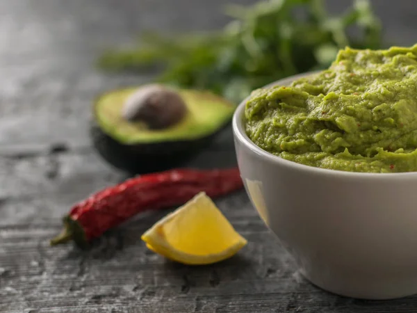 White bowl with guacamole, lemon, tomatoes and garlic on a rustic table. Diet vegetarian Mexican food avocado. — Stock Photo, Image