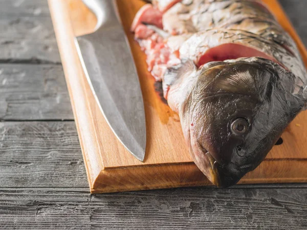 Cut into pieces carp fish with a knife on a cutting Board.