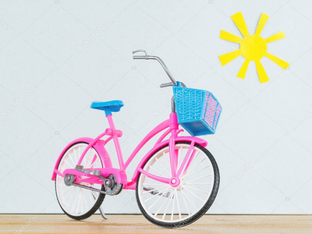 Pink model of children's Bicycle on the wooden floor against the background of the toy sun.