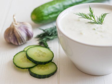 Taze salatalık Beyaz ahşap bir masa üzerinde beyaz bir kase cacık yaptı.