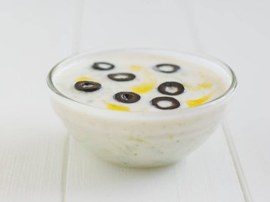 Beyaz ahşap bir masa üzerinde zeytinli dekore edilmiş Tzatziki sos kase.