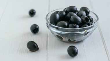 Beyaz ahşap bir masa üzerinde bir cam kase konserve zeytin.