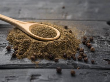 Çekilmiş karabiber rustik bir karanlık tabloda tüm biber yığını üzerinde tahta kaşıkla.