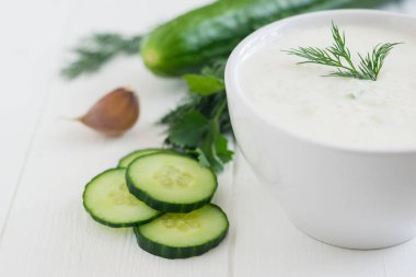 Taze salatalık ve sarımsak Beyaz ahşap bir masa üzerinde beyaz bir kase cacık yaptı.