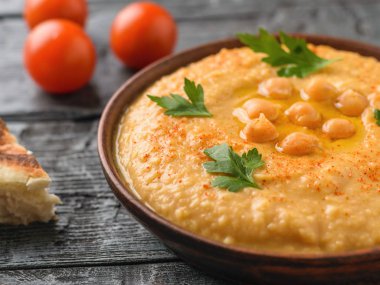 Bir kase taze yapılmış humus ve rustik bir tabloda kiraz domates.