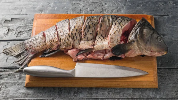 Свежая речная рыба на доске с большим ножом на темном деревянном столе . — стоковое фото