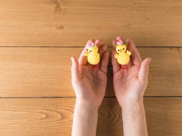 Two small toy chicken in the hands of a child on a wooden table.