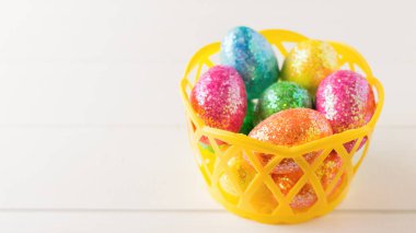 Beyaz rustik ahşap masa üzerinde renkli yumurta ile sarı sepeti.