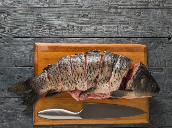 Cut into pieces carp fish with a knife on a black table. Place for your text.
