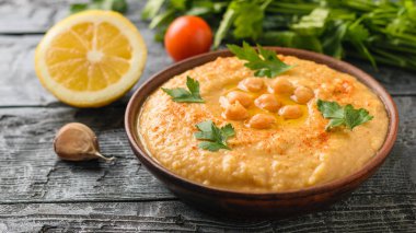 Bir parça ekmek ile rustik bir tabloda bir kil kahverengi kase taze yapılmış humus.