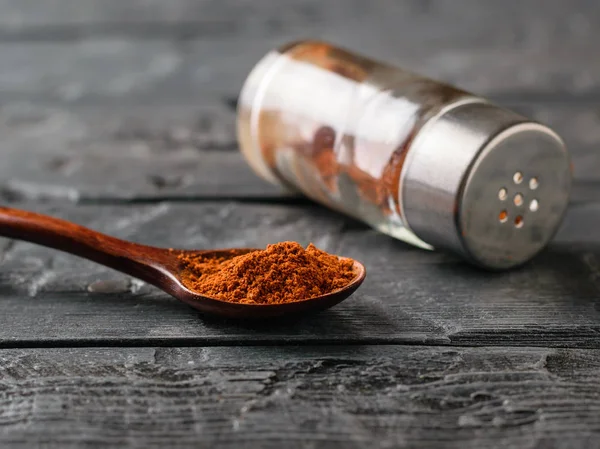 Wooden spoon and a jar of red pepper powder on a dark rustic table.