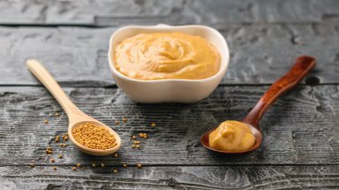 Hardal tohumu, hardal sosu ve karanlık rustik masada beyaz kase kaşık kaşık.