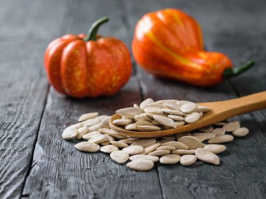 Tahta kaşıkla kabak çekirdeği ve rustik masada iki kabak meyve.