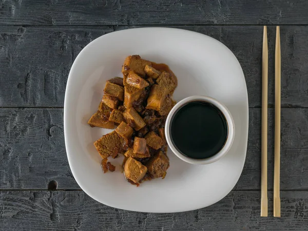 A bowl of tofu and soy sauce on a wooden table. Flat lay.