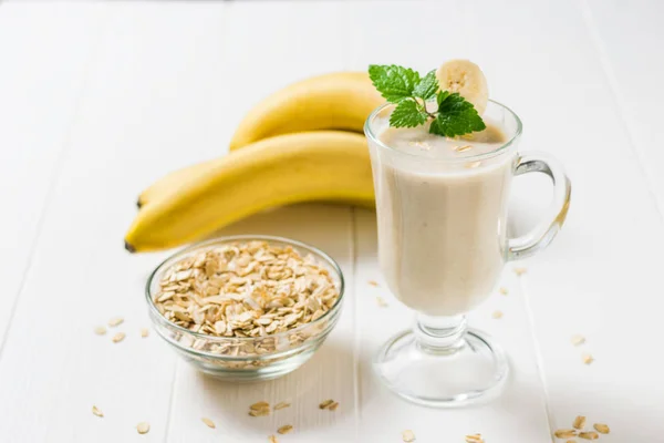 Smoothie dalam gelas, oatmeal dan pisang di atas meja putih. Vegetarian smoothie . — Stok Foto