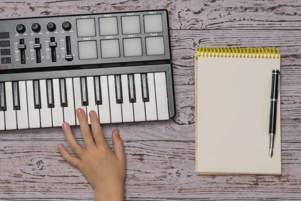 Een hand op een muziekmixer en een notitieboekje met een pen op een houten tafel. Het proces van muziek maken. Het uitzicht vanaf de top. — Stockfoto