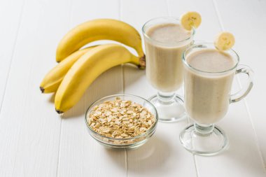 Three bananas and glasses of oatmeal and banana smoothies on a white table. Vegetarian smoothie.