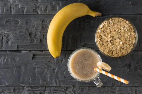 Pisang, oatmeal dan segelas smoothie di atas meja kayu. Letak rata . — Stok Foto