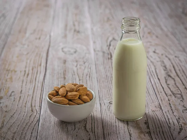 Un tazón de almendras y una botella de leche de almendras en una mesa de madera . — Foto de Stock