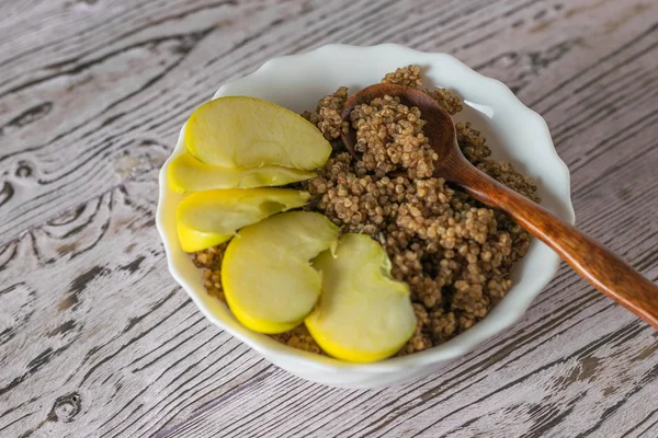 Wooden spoon and Apple slices in a bowl of quinoa porridge. — Stock Photo, Image