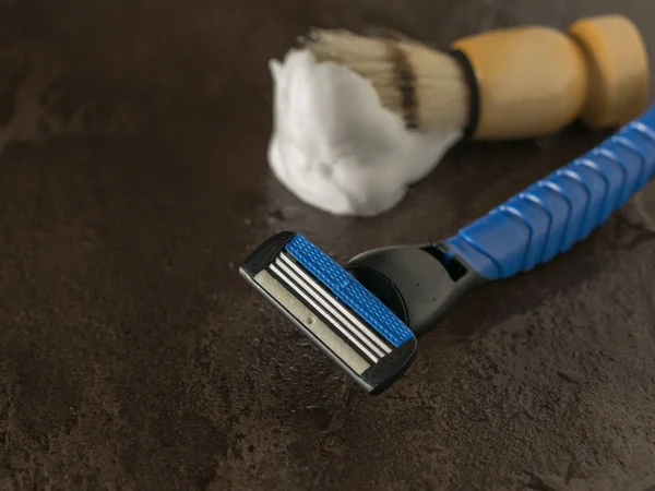 Shaving brush with foam and blue men\'s razor on a stone background. Flat lay.