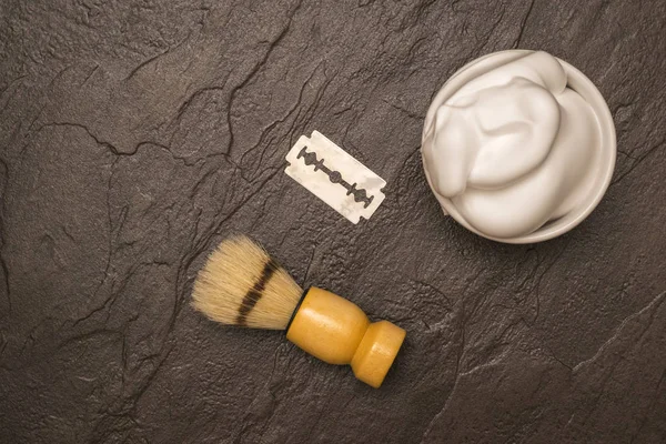 Shaving brush, shaving foam, and a blade on a stone table. Flat lay.