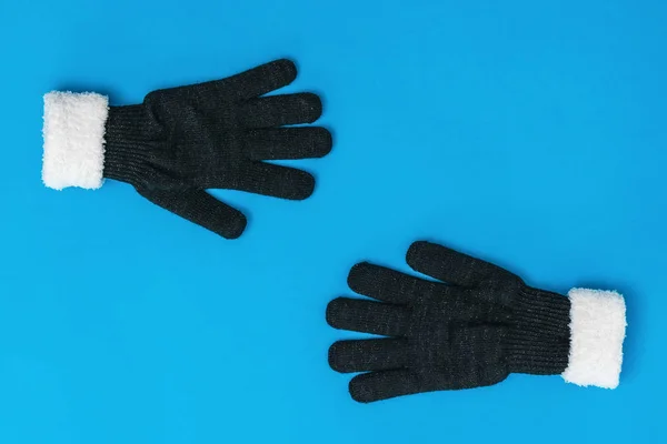 Black and white knitted gloves reach out to each other on a blue background. The concept of hope and meeting.