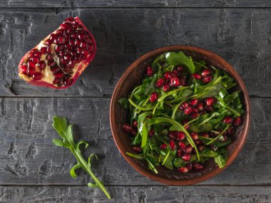 Arugula, nar tohumları ve zeytin yağıyla ahşap bir masada kil kasede. Düz yatıyordu.