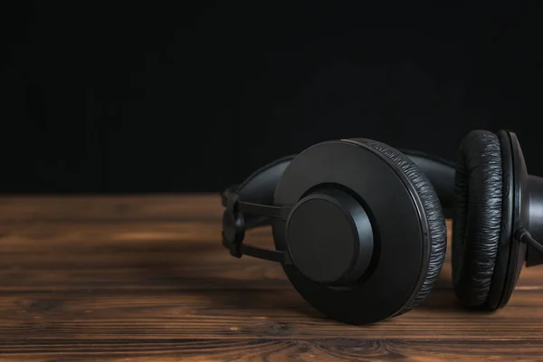 Beautiful black headphones on wooden table on black background.