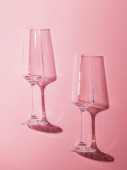 Dvě prázdné sklenice šampaňského na růžovém pozadí v ostrém světle.